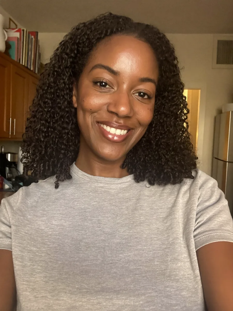 Casual phone selfie of an AI-generated woman in a grey t-shirt in a kitchen, the reference photo